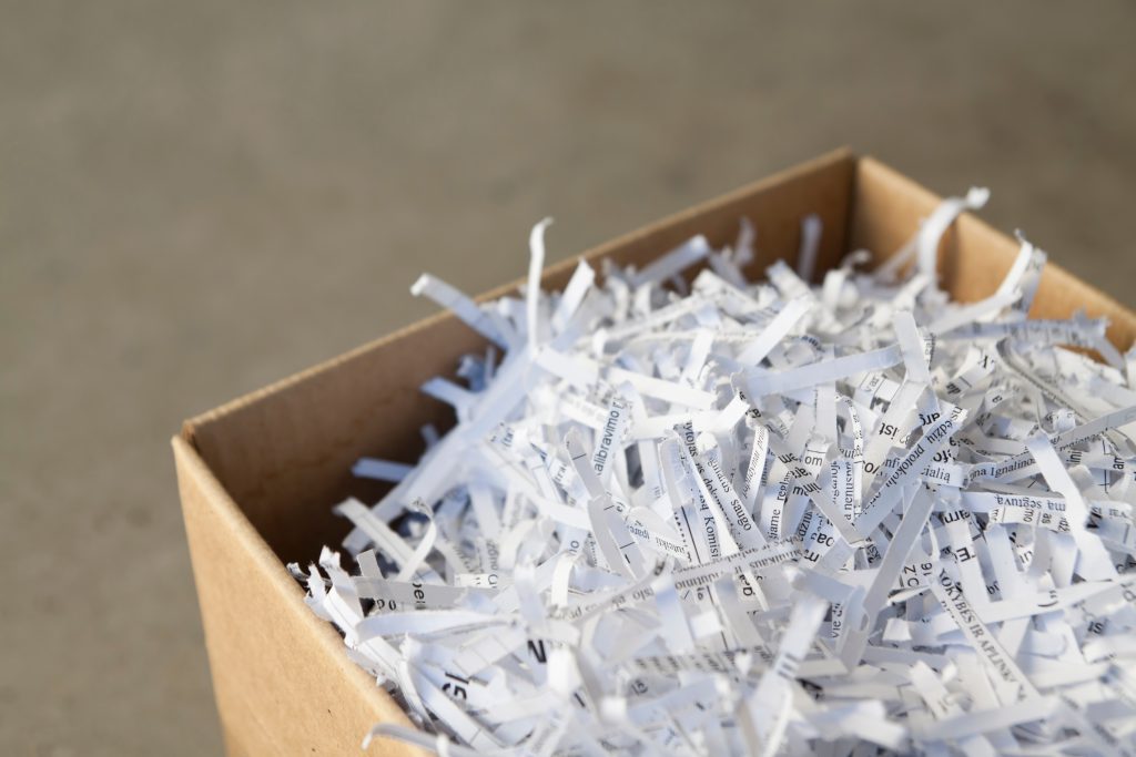 A cardboard box filled with shredded paper strips, displaying fragments of printed text. The image conveys a sense of recycling or document disposal.